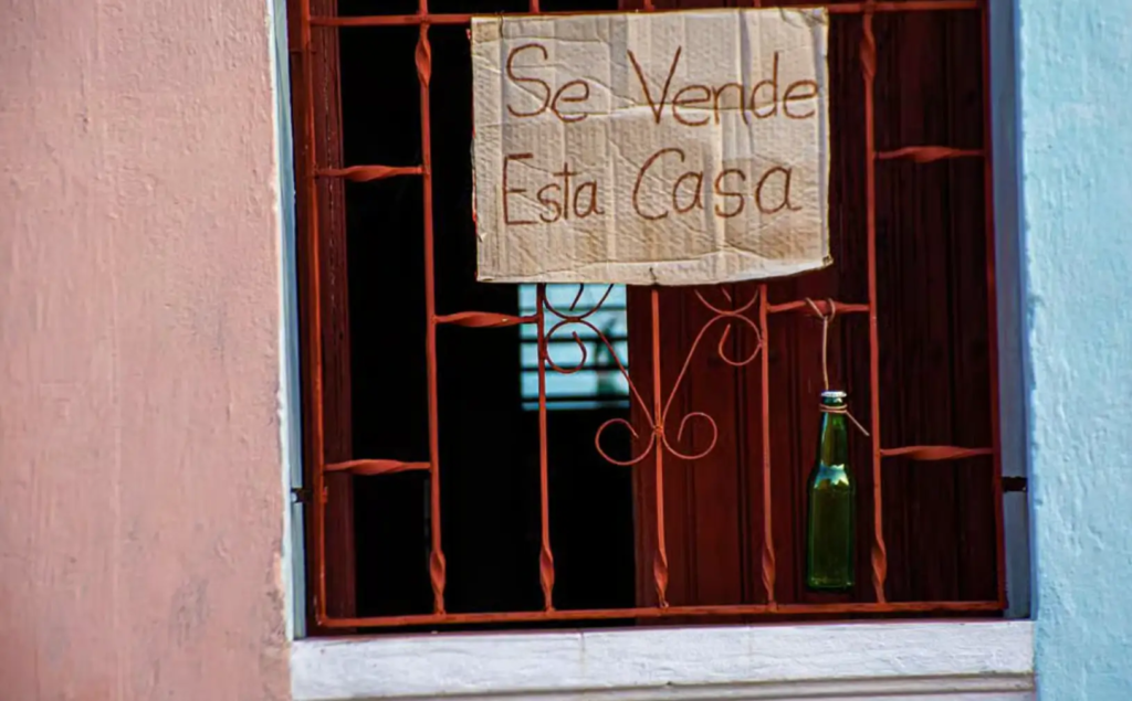 una ventana de una casa en cuba , un cartel muestra q la casa esta en vneta, el cartel esta escrito a mano sobre un carton de caja