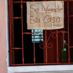 una ventana de una casa en cuba , un cartel muestra q la casa esta en vneta, el cartel esta escrito a mano sobre un carton de caja