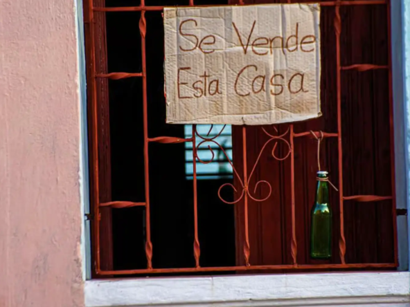 una ventana de una casa en cuba , un cartel muestra q la casa esta en vneta, el cartel esta escrito a mano sobre un carton de caja